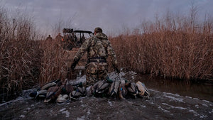A duck hunter in Valo camouflage pulling duck decoys through shallow water while with other hunters load a UTV.