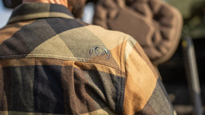 Close-up of a person wearing a Field Flannel Shirt, showing the back of the neck and a small KUIU Ram embroidered logo on the shoulder.