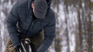 A man wearing a KUIU Super Down Jacket in Gunmetal Grey bent over in a snowy outdoor setting.