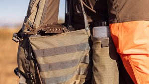 Close-up of a Upland Field Vest in Khaki worn over the shoulder, with a bird tucked inside the side pouch.