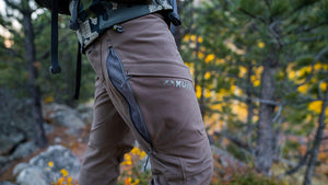 A man hiking through a rugged, vegetative talus environment in KUIU Attack Pants in Major Brown.
