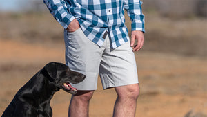 Man standing beside his black lab while wearing KUIU shorts and a Borrego Long Sleeve Shirt.
