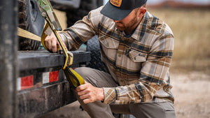 A man wearing the KUIU Field Flannel tightens a ratchet strap on his trailer.