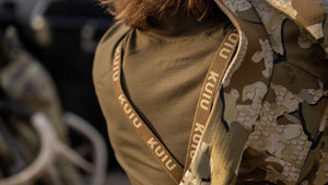 Close-up of a male throwing on his jacket over his hunting shirt and Proximity pant suspenders.