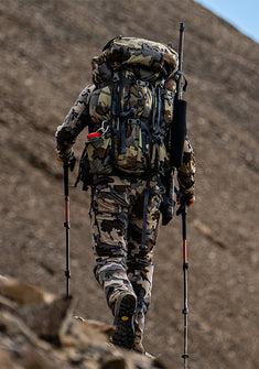 Back of a hunter trekking on a bare, rock-covered mountain slope