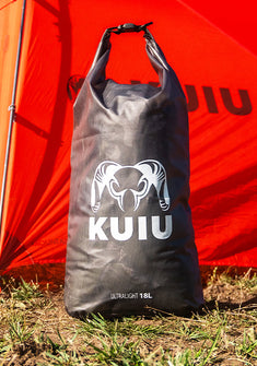 Front of HD Roll Top Dry Bag in Stone Grey, shown placed on the grass in front of Mountain Star 2 Person Tent in Gunmetal-Orange