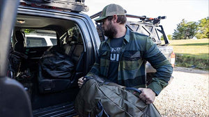 Rugged male throwing his KUIU Travel Gear into the back of his truck in a KUIU Field Flannel.
