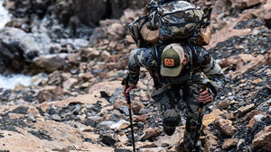 Male in head to toe KUIU Vias Camo gear trekking up a hill alongside a river.