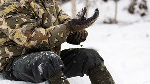 Male hunter utilizing the KUIU layering system in the snow, adjusting his insulated gloves.