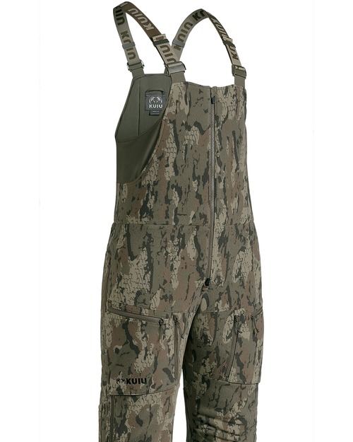 A Veros camouflage bib overalls with a digital tree bark pattern in shades of green, brown, and beige, featuring adjustable shoulder straps, a front zipper, and multiple utility pockets, shown against a plain white background.