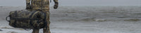 Side of hunter carrying a Taku Blstx Duffel on a rocky beach.