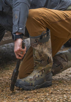Man kneeling next to an UTV, wearing KUIU HD Mud Boot in Vias Camouflage