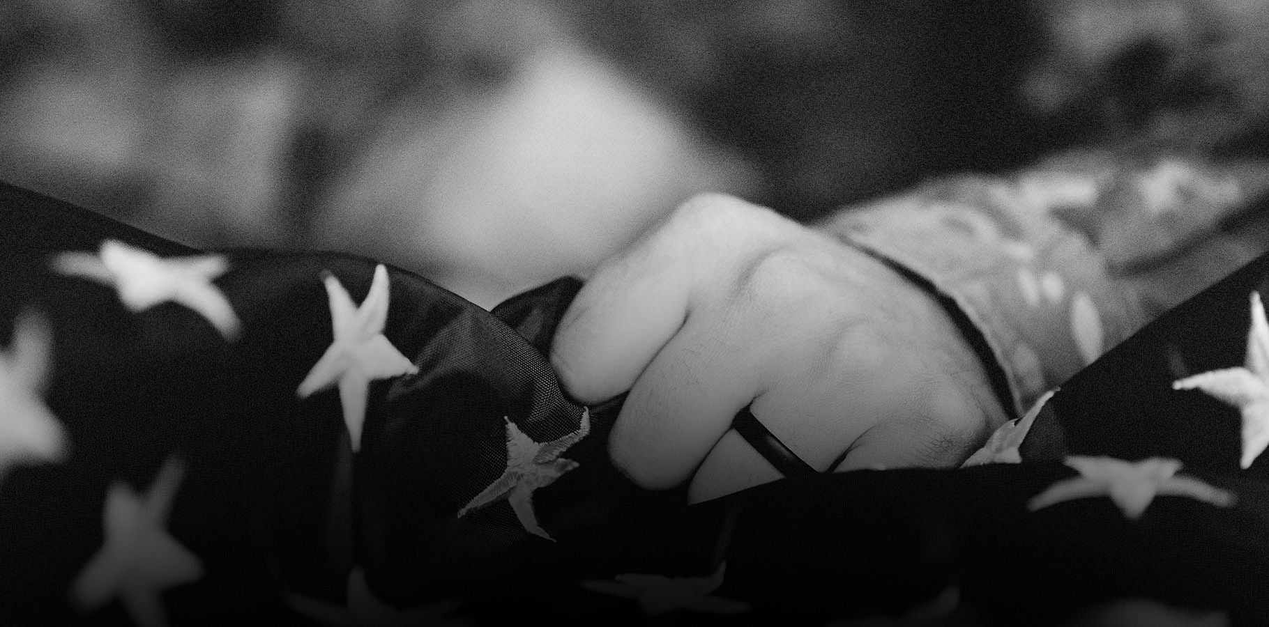 Black and white image of a veterans fist and wedding ring holding onto a USA flag.