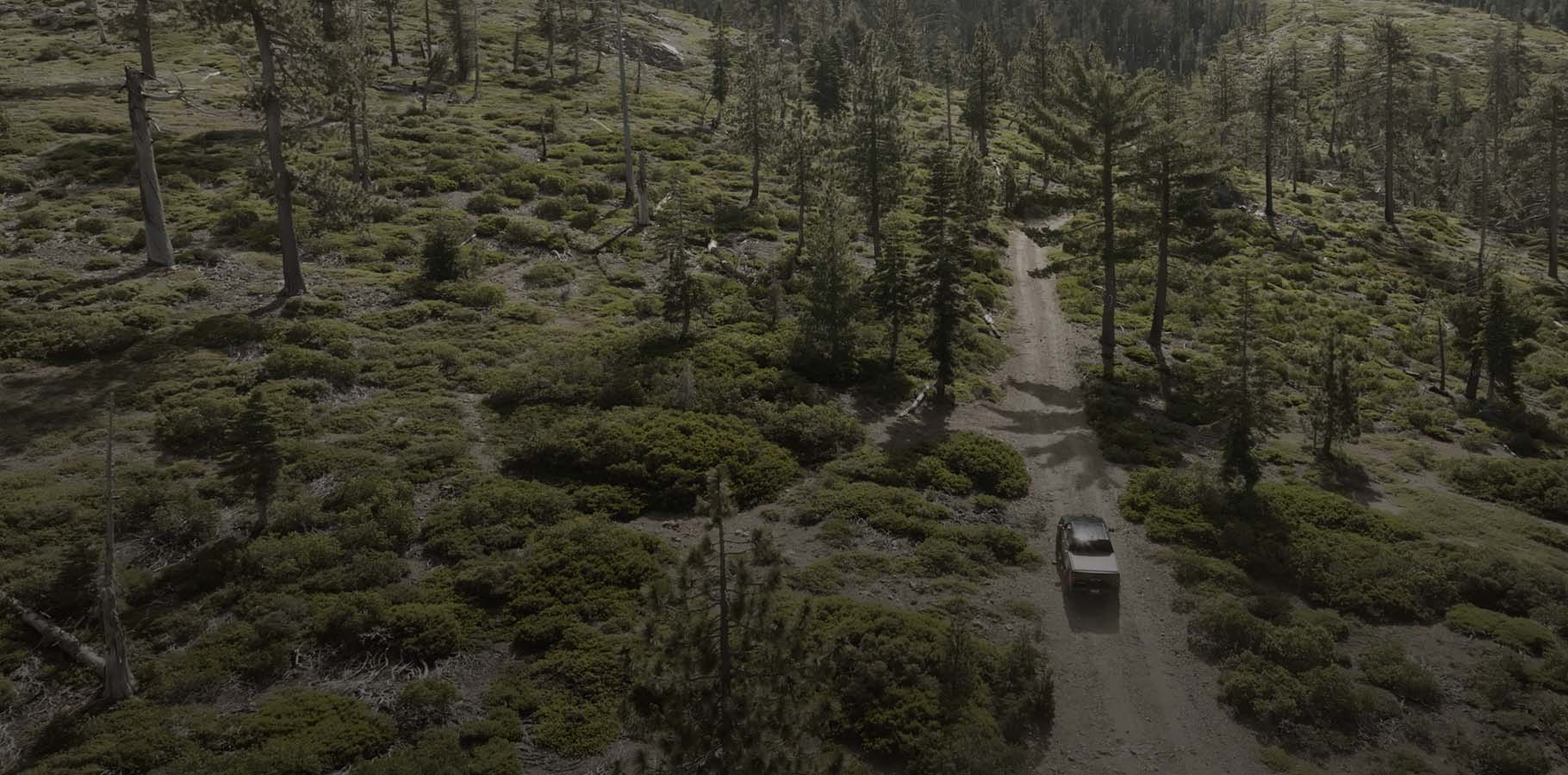 Backcountry hunting truck driving on a rugged high-mountain dirt road at dusk.