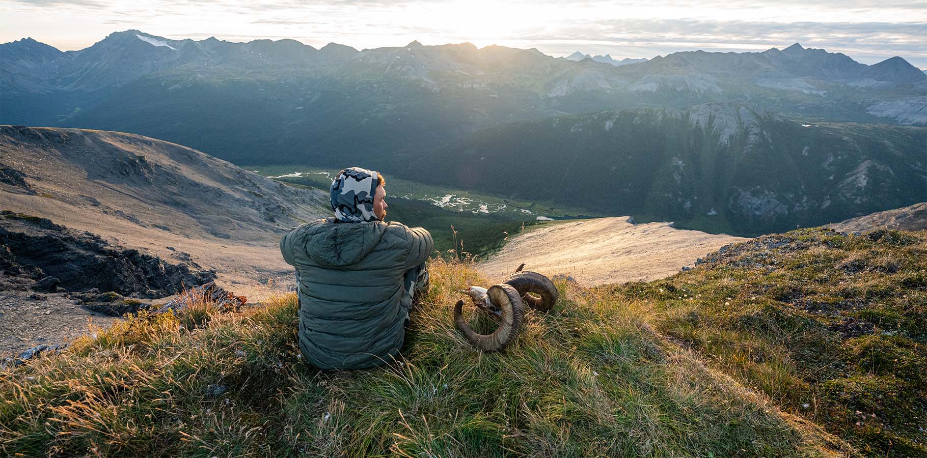 A hunter sitting on top of a mountain as the sun sets.