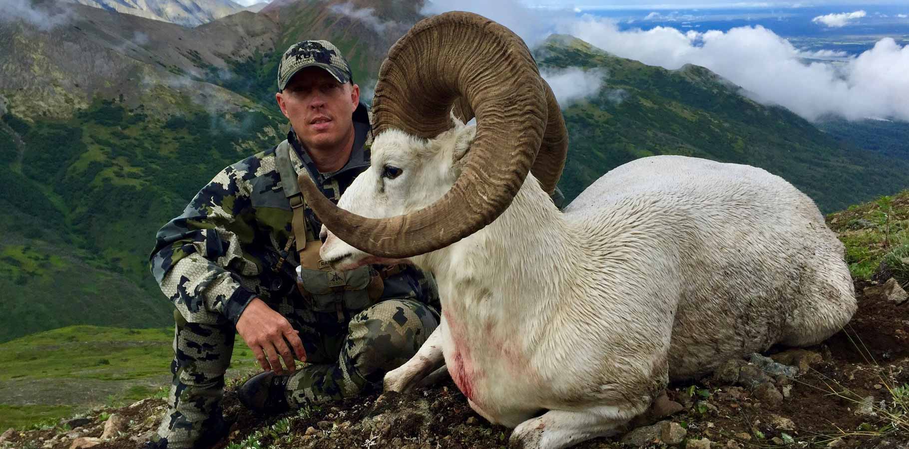 Justin Shaffer in Verde camouflage kneeling behind another of his Dall Sheep that he harvested with his archery equipment