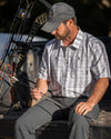 Hunter sitting on tailgate of his truck, looking down at his arrow, wearing Borrego SS Shirt in Grey Granite Plaid
