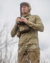 Hunter holding binoculars wearing the Gila PRO LS Hoodie in Khaki with hood on