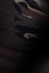 Close-up of a Veros camouflage, textured fabric with a subtle woven pattern, shown in very low light with soft focus.