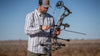 Hunter in an outdoor setting adjusting his bow and arrow, wearing Borrego LS Shirt in Grey Granite Plaid
