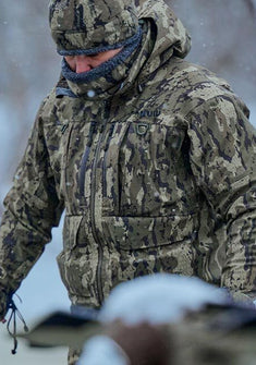 Hunter wearing Vero camouflage gear, standing outdoors in snowy weather.