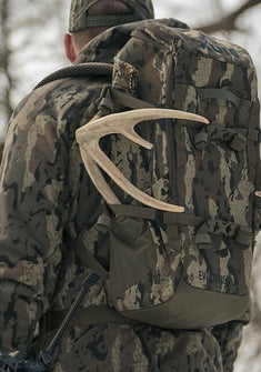 Close-up of a hunter in matching Veros camouflage outdoor gear carrying Veros camouflage Evolution 1800 hunting backpack with a large antler attached to the side.