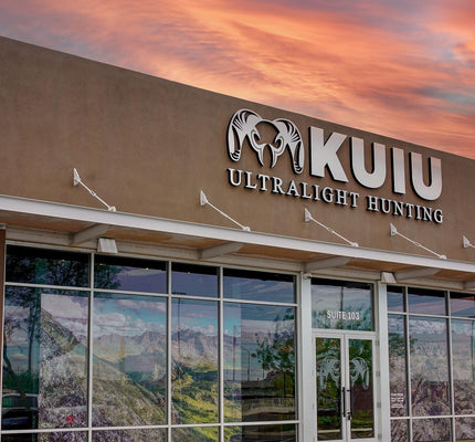 Tempe, Arizona, KUIU Ultralight Hunting storefront exterior at sunset, with a tan building facade, large glass windows, and a dramatic orange-pink sky reflected in the windows.