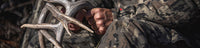 A close-up lifestyle shot of a person in Veros camouflage hunting clothing holding a large antlered hunting trophy.