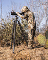 Youth hunter standing, wearing Youth Gila LS Hoodie in Valo Camouflage, glassing using tripod
